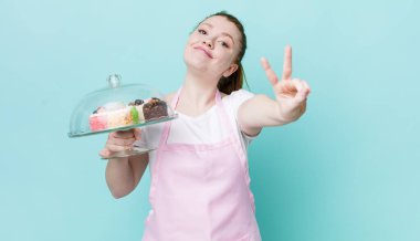 Kızıl saçlı güzel kadın gülümsüyor ve mutlu görünüyor, zafer ya da barış işareti yapıyor. Ev yapımı kek konsepti