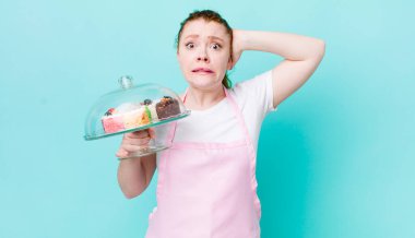 Kızıl saçlı güzel kadın stresli, endişeli ya da korkmuş, elleri başının üstünde. Ev yapımı kek konsepti