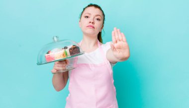 Kızıl saçlı güzel kadın ciddi görünüyor. Avuç içini gösteriyor. Durdurma hareketi yapıyor. Ev yapımı kek konsepti