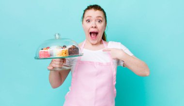 Kızıl saçlı güzel bir kadın mutlu hissediyor ve heyecanla kendini işaret ediyor. Ev yapımı kek konsepti