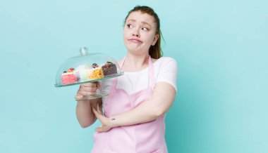 Kızıl saçlı güzel kadın omuz silkiyor, kafası karışık ve kararsız. Ev yapımı kek konsepti