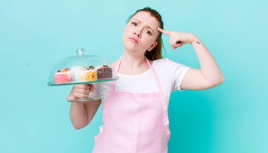 Kızıl saçlı güzel kadın kafası karışık ve şaşkın hissediyor, deli olduğunu gösteriyor. Ev yapımı kek konsepti