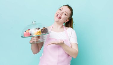 kızıl saçlı güzel bir kadın neşeli bir şekilde gülümsüyor, mutlu hissediyor ve bir konsept gösteriyor. Ev yapımı kek konsepti