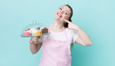 Kızıl saçlı, güzel bir kadın kendi gülüşünü işaret ediyor. Ev yapımı kek konsepti