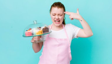 Kızıl saçlı güzel bir kadın mutsuz ve stresli görünüyor, intihar jesti silah işareti yapıyor. Ev yapımı kek konsepti