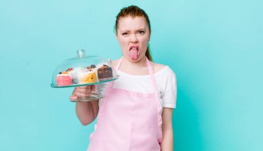 Kızıl saçlı güzel kadın iğrenmiş ve sinirlenmiş hissediyor ve dilini dışarı çıkarıyor. Ev yapımı kek konsepti