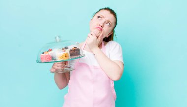 Kızıl saçlı güzel kadın düşünüyor, kuşkulu ve şaşkın hissediyor. Ev yapımı kek konsepti