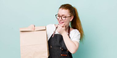 Kızıl saçlı, güzel bir kadın mutlu, kendinden emin, elleri çenesinde gülümsüyor. teslimat kavramını kaldır