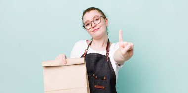 Kızıl saçlı güzel kadın gülümsüyor ve arkadaş canlısı görünüyor, bir numarayı gösteriyor. teslimat kavramını kaldır