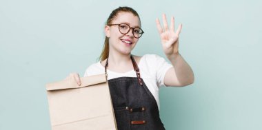 Kızıl saçlı güzel kadın gülümsüyor ve arkadaş canlısı görünüyor, dört numarayı gösteriyor. teslimat kavramını kaldır