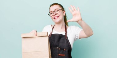 Kızıl saçlı güzel kadın gülümsüyor ve arkadaş canlısı görünüyor, beş numarayı gösteriyor. teslimat kavramını kaldır