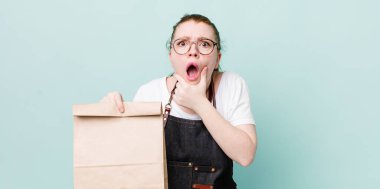 Kızıl saçlı, ağzı ve gözleri açık, eli çenesinde güzel bir kadın. teslimat kavramını kaldır