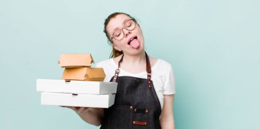 Kızıl saçlı, güzel, neşeli ve asi tavırlı, şaka yapan ve dilini dışarı çıkaran bir kadın. teslimat kavramını kaldır