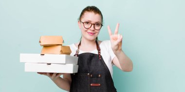 Kızıl saçlı güzel kadın gülümsüyor ve arkadaş canlısı görünüyor, iki numarayı gösteriyor. teslimat kavramını kaldır