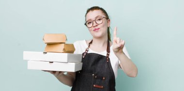 Kızıl saçlı güzel kadın gülümsüyor ve arkadaş canlısı görünüyor, bir numarayı gösteriyor. teslimat kavramını kaldır