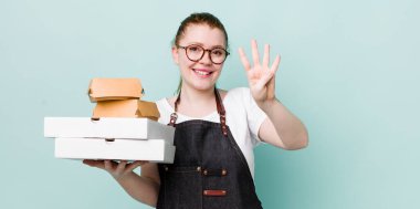 Kızıl saçlı güzel kadın gülümsüyor ve arkadaş canlısı görünüyor, dört numarayı gösteriyor. teslimat kavramını kaldır