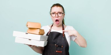 Kızıl saçlı güzel kadın şok olmuş ve ağzı açık, kendini işaret eden bir şekilde şaşırmış görünüyor. teslimat kavramını kaldır