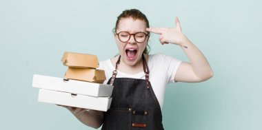 Kızıl saçlı güzel bir kadın mutsuz ve stresli görünüyor, intihar jesti silah işareti yapıyor. teslimat kavramını kaldır