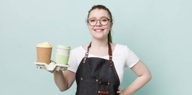 Kızıl saçlı güzel kadın mutlu bir şekilde gülümsüyor, eli kalçasında ve kendinden emin. kahve konseptini kaldır.