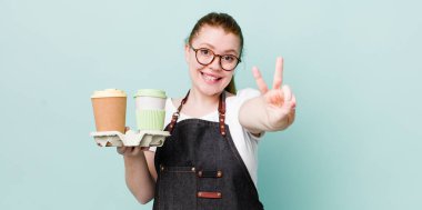 Kızıl saçlı güzel kadın gülümsüyor ve mutlu görünüyor, zafer ya da barış işareti yapıyor. kahve konseptini kaldır.