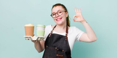 Kızıl saçlı güzel bir kadın kendini mutlu hissediyor. Onayını iyi bir hareketle gösteriyor. kahve konseptini kaldır.