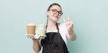 Kızıl saçlı güzel kadın gülümsüyor ve arkadaş canlısı görünüyor, iki numarayı gösteriyor. kahve konseptini kaldır.