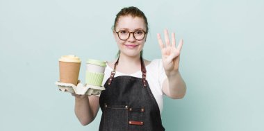 Kızıl saçlı güzel kadın gülümsüyor ve arkadaş canlısı görünüyor, dört numarayı gösteriyor. kahve konseptini kaldır.