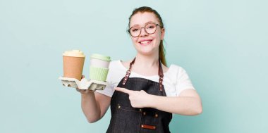 Kızıl saçlı güzel bir kadın neşeyle gülümsüyor, mutlu hissediyor ve bir tarafı işaret ediyor. kahve konseptini kaldır.