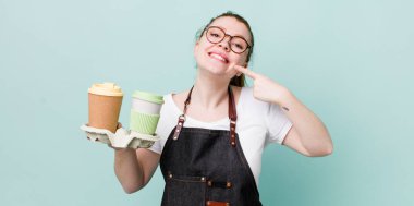 Kızıl saçlı, güzel bir kadın kendi gülüşünü işaret ediyor. kahve konseptini kaldır.