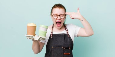 Kızıl saçlı güzel bir kadın mutsuz ve stresli görünüyor, intihar jesti silah işareti yapıyor. kahve konseptini kaldır.