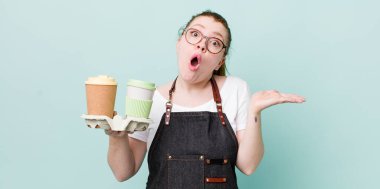 Kızıl saçlı, güzel bir kadın şaşırmış ve şok olmuş görünüyor. Çenesi düşmüş, elinde bir nesne var. kahve konseptini kaldır.