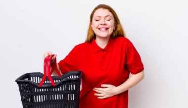 Kızıl saçlı güzel bir kadın komik bir şakaya yüksek sesle gülüyor. boş alışveriş sepeti kavramı