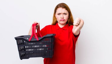 Kızıl saçlı, güzel bir kadın kendini kötü hissediyor, baş parmağını kaldırıyor. boş alışveriş sepeti kavramı