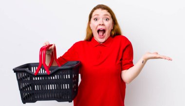 Kızıl saçlı güzel kadın kendini mutlu hissediyor ve inanılmaz bir şeye hayret ediyor. boş alışveriş sepeti kavramı