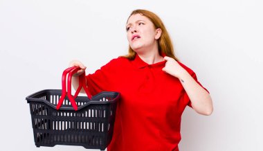 Kızıl saçlı güzel kadın stresli, endişeli, yorgun ve hayal kırıklığına uğramış hissediyor. boş alışveriş sepeti kavramı