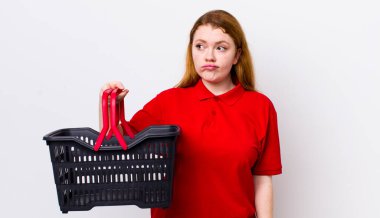 Kızıl saçlı, güzel bir kadın üzgün, üzgün ya da kızgın ve yana bakıyor. boş alışveriş sepeti kavramı