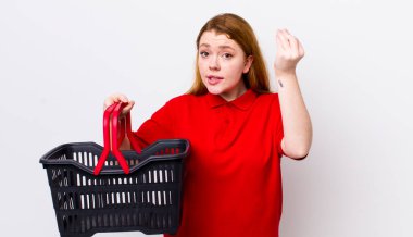 Kızıl saçlı, güzel bir kadın kapiş ya da para hareketi yapıyor, sana ödemeni söylüyor. boş alışveriş sepeti kavramı