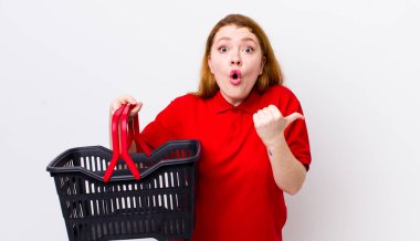 Kızıl saçlı, güzel bir kadın inançsızlıktan şaşkın şaşkın bakıyor. boş alışveriş sepeti kavramı