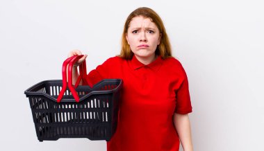 Kızıl saçlı, güzel bir kadın üzgün ve mızmızlanıyor. Mutsuz bir bakışı var ve ağlıyor. boş alışveriş sepeti kavramı