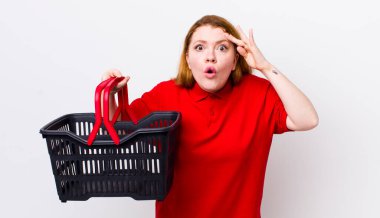 Kızıl saçlı güzel kadın şaşırmış görünüyor, yeni bir düşünce, fikir ya da konsept fark ediyor. boş alışveriş sepeti kavramı