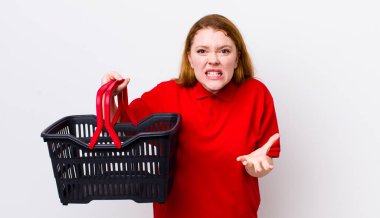 Kızıl saçlı, güzel bir kadın sinirli, sinirli ve sinirli görünüyor. boş alışveriş sepeti kavramı