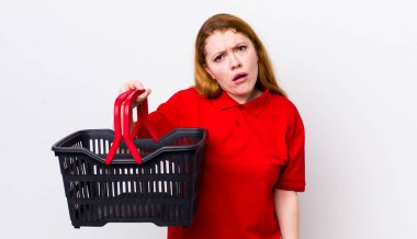 Kızıl saçlı güzel kadın şaşkın ve şaşkın hissediyor. boş alışveriş sepeti kavramı