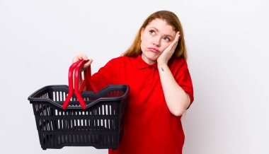 Kızıl saçlı, güzel bir kadın bıkkın, yorgun ve uykulu hissediyor. boş alışveriş sepeti kavramı