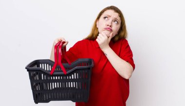 Kızıl saçlı güzel kadın düşünüyor, kuşkulu ve şaşkın hissediyor. boş alışveriş sepeti kavramı