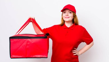 Kızıl saçlı güzel kadın mutlu bir şekilde gülümsüyor, eli kalçasında ve kendinden emin. Pizza teslimatı kavramı