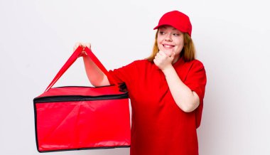 Kızıl saçlı, güzel bir kadın mutlu, kendinden emin, elleri çenesinde gülümsüyor. Pizza teslimatı kavramı