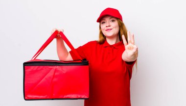 Kızıl saçlı güzel kadın gülümsüyor ve arkadaş canlısı görünüyor, üç numarayı gösteriyor. Pizza teslimatı kavramı