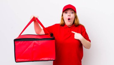 Kızıl saçlı güzel kadın şok olmuş ve ağzı açık, kendini işaret eden bir şekilde şaşırmış görünüyor. Pizza teslimatı kavramı