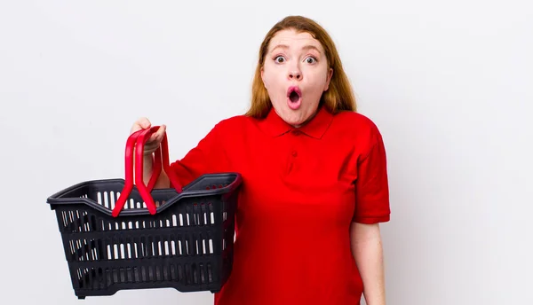 红头发漂亮的女人看上去非常震惊或惊讶 空购物篮概念 — 图库照片