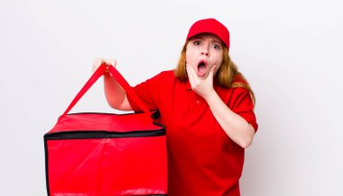 Kızıl saçlı, ağzı ve gözleri açık, eli çenesinde güzel bir kadın. Pizza teslimatı kavramı